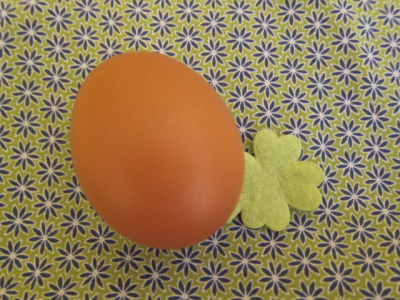 Hühnerei mit gelbem Filz-Kleeblatt auf gelbem Stoff mit bleuaen Blümchen 