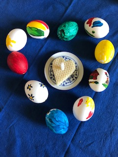 bunt bemalte Eier als Herz gelegt, in der Mitte ein herzförmiges Kuchenstück mit einer Kerze