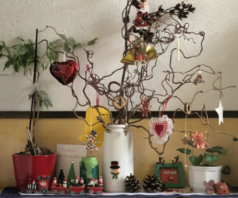 Zweige in Vase mit Anhängern. Adventsdekorationen im Vordergrund.Rechts und links der Vase Topfpflanzen.