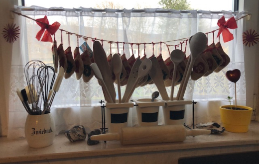 Adventsgirlande (aus 24 Rupfenstiefelchen) am Küchenfenster. Im Vordergrund Gefäße mit Holzkochlöffeln, Schneebesen und Nudelholz