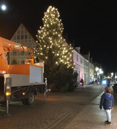 Fussgängerzone mit großem, erleuchteten Tannenbaum, Vollmond und Kind, dass hoch zum Baum schaut und Mond.